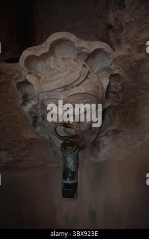 Primo piano di un'antica fontana in pietra con un beccuccio di metallo nel monastero di Alcoba Foto Stock