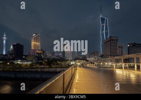 Vista notturna dal ponte pedonale alla stazione LRT di Masjid Jamek nel centro di Kuala Lumpur con grattacielo Merdeka 118 illuminato sullo sfondo Foto Stock
