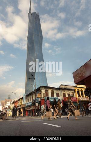 I pedoni attraversano una strada trafficata nel quartiere Chinatown di Kuala Lumpur, Malesia, con il grattacielo Merdeka 118 che domina lo skyline Foto Stock