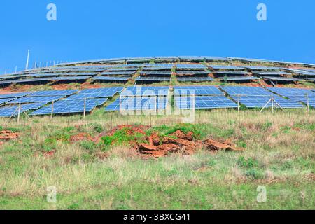 File di pannelli solari si estendono su una collina illuminata dal sole, angolata per catturare la luce del sole. La scena riflette l'impegno per le energie rinnovabili Foto Stock