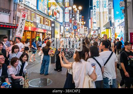 Un'intensa scena serale nel famoso quartiere Dotonbori di Osaka, in Giappone. Folle di persone camminano attraverso i vivaci ristoranti e i negozi pieni di strade. Foto Stock