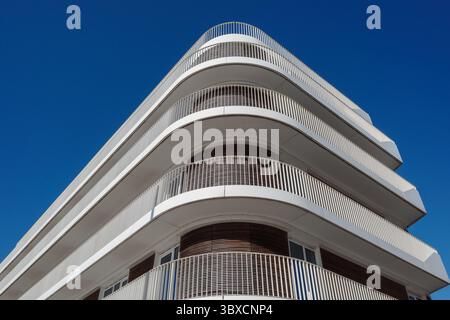 Un basso angolo con vista a verme dell'esterno di un moderno edificio di appartamenti bianco. Il design architettonico presenta prominenti balconi curvi. Foto Stock