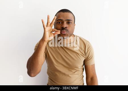 Uomo nero giocoso che gestiva le labbra con le dita, esprimendo silenzio o segretezza Foto Stock