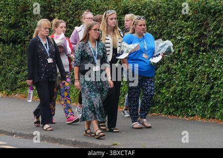 Un gruppo arriva portando fiori per deporre con i tributi floreali all'ingresso della Minehead Middle School di Minehead nel Somerset. Un bambino è morto e diverse persone sono state curate in ospedale per lesioni gravi dopo che un pullman che trasportava bambini e personale dalla casa scolastica si è ribaltato sul suo tetto e ha scivolato giù una riva di 20 piedi sulla A396 Cutcombe Hill, tra Wheddon Cross e Timbercombe giovedì. Data foto: Venerdì 18 luglio 2025. Foto Stock