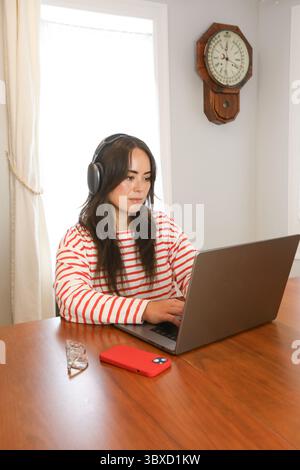 Donna che indossa le cuffie wireless mentre lavora da casa Foto Stock