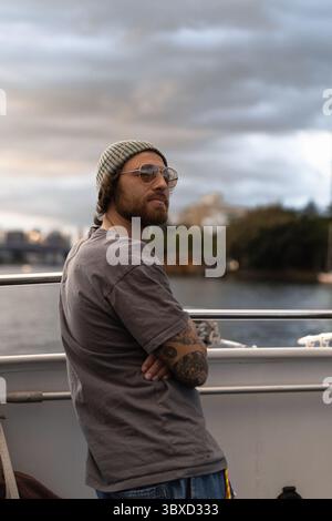 Uomo con barba e tatuaggi sui traghetti al tramonto, trasporto a Brisbane Foto Stock
