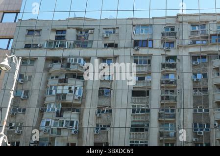 Architettura urbana vecchia e nuova. Vecchio edificio di appartamenti che si riflette su una parete di vetro di un edificio moderno di uffici a Bucarest Foto Stock