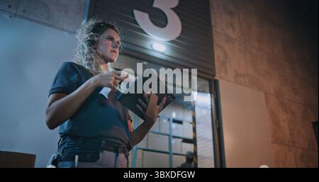 Dipendenti diversi che trasportano scatole di cartone dal magazzino di distribuzione logistica di notte. Responsabile donna che esegue la scansione di pacchi con scanner di codici a barre, utilizzando un tablet digitale. Ordini online, merci, consegna. Foto Stock