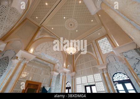 Interni lussuosi con colonne in marmo ornate e un intricato design del soffitto caratterizzato da un grande lampadario. Foto Stock