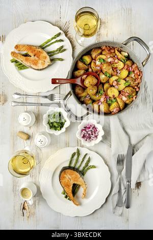 Un tavolo da pranzo ben organizzato presenta due piatti di salmone alla griglia serviti con patate arrosto e asparagi. Due bicchieri di vino bianco Foto Stock