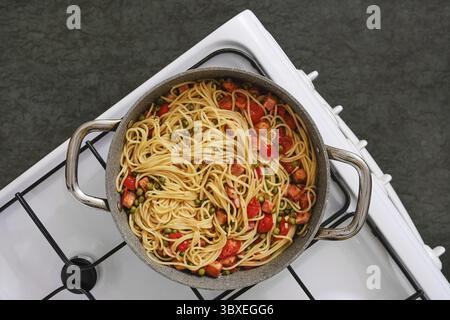 Vista dall'alto di una pentola ripiena di pasta appena cucinata con pancetta e pomodori su un piano cottura. L'aroma invitante riempie l'accogliente cucina mentre si prepara Foto Stock