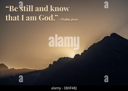 L'immagine è una catena montuosa con un tramonto sullo sfondo. La citazione "siate fermi e sappiate che io sono Dio" è scritta sotto l'immagine. La scena è pacifica Foto Stock