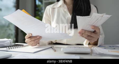 Una persona detiene moduli fiscali e rivede documenti finanziari, concentrandosi sull'importanza della preparazione fiscale Foto Stock
