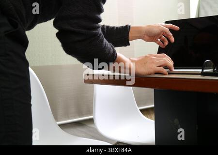 Un designer lavora su un computer portatile presso una scrivania in legno in un moderno spazio di lavoro. Le mani stanno digitando e puntando verso lo schermo, mostrando un lavoro creativo e mirato Foto Stock