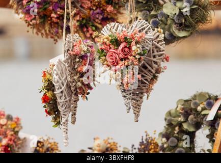 Ornamenti rustici a forma di cuore fatti di ramoscelli naturali e adornati con fiori secchi, catturati in un mercato locale all'aperto. Perfetto per l'arredamento stagionale o. Foto Stock