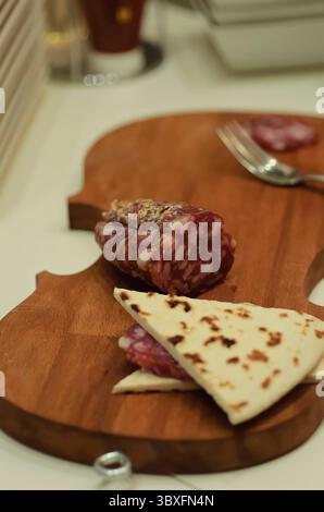 Una deliziosa esperienza culinaria con salumi artigianali e focaccine servite su una tavola di legno unica a forma di violino che cattura l'essenza di Foto Stock