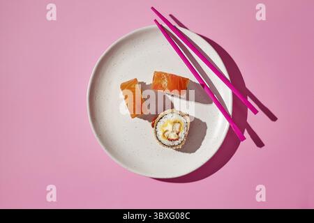 Sushi panini appena fatti serviti su un piatto con bacchette rosa, creando una vivace e appetitosa scena culinaria Foto Stock