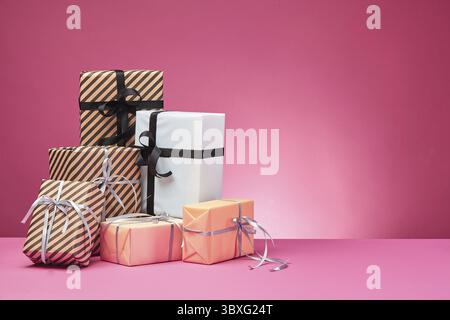 Dimensioni differenti, colorati a strisce e pianura, marrone, rosa e bianco presente carta scatole legate con nastri multicolori e archi su una superficie di colore rosa e Foto Stock