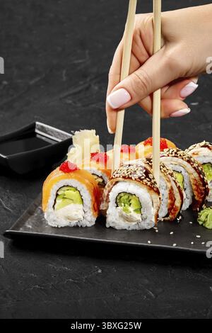 Donna che usa le bacchette che raccoglie i panini di sushi uramaki philadelphia con salmone, avocado, formaggio spalmabile e caviale rosso Foto Stock
