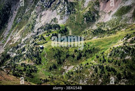 Vista aerea di un tranquillo paesaggio montano caratterizzato da un piccolo lago circondato da vegetazione lussureggiante e terreno roccioso. Vicino al wa è visibile una pittoresca cabina Foto Stock