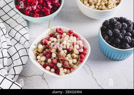 Cibo, ribes rosso e bianco congelati in un recipiente e altre bacche sul tavolo Foto Stock