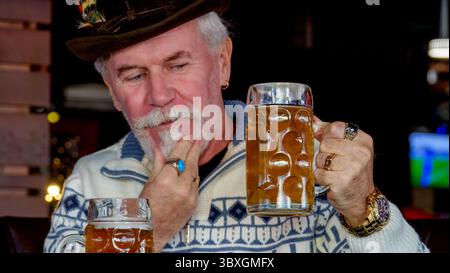 Un uomo anziano dai capelli grigi barbuti bello in una birreria sta riposando Foto Stock