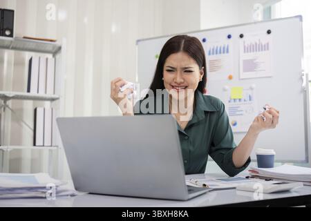 Giovane donna d'affari asiatica che lavora su un notebook, è stressata ha mal di testa e pensa duramente in ufficio Foto Stock