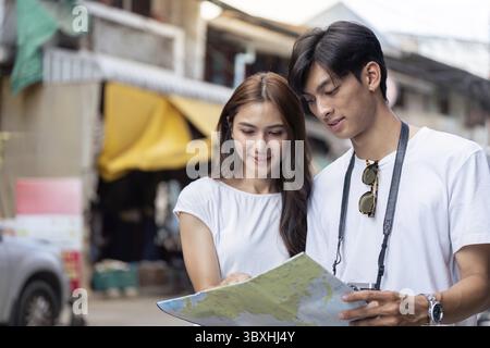 Felice giovane coppia asiatica che cammina attraverso un vivace mercato, intrecciando le mani mentre assorbi le vivaci immagini e i suoni che li circondano Foto Stock