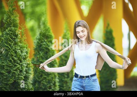 Una giovane adolescente che cammina per la strada in jeans e con un maglione in una giornata estiva. Il concetto di moda giovanile. Stile di vita urbano Foto Stock