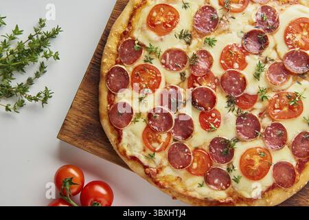 Parte della pizza italiana al peperoni fatta in casa con salame, mozzarella su tavola bianca, cena rustica con salsiccia e pomodori, vista laterale Foto Stock