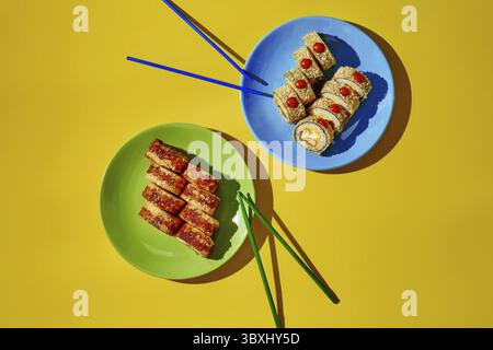 Sushi fritti caldi con semi di sesamo serviti su piatti con bacchette su sfondo giallo, pronti per essere consumati Foto Stock