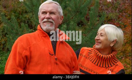 Felice anziani bella coppia sposata con i capelli grigi in arancione sportswear su uno sfondo di autunno alberi con foglie di giallo Foto Stock