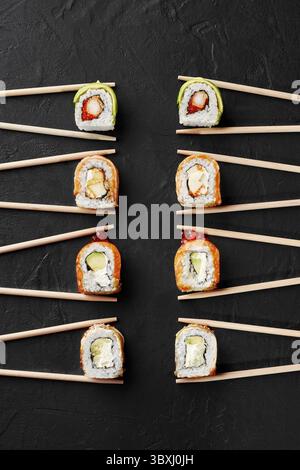 Vari appetitosi sushi Rolls con salmone, anguilla, gamberi, avocado e caviale in bacchette su superficie ruvida nera, vista dall'alto. Concetto di popolarità o Foto Stock