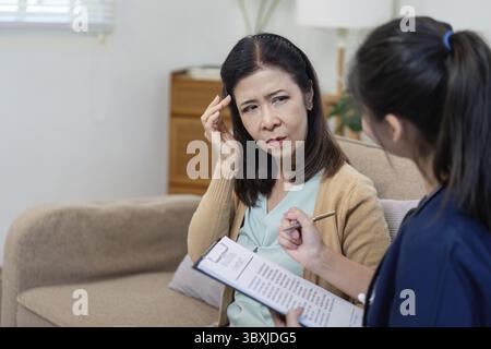 Un operatore sanitario valuta i sintomi di un paziente anziano durante un check-up evidenziando l'importanza delle interazioni sanitarie Foto Stock