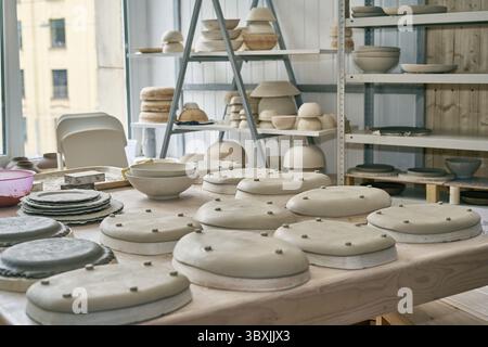 Fabbricazione di prodotti ceramici, pezzi in lavorazione. Primo piano di sfondo con pezzi di ceramica sul tavolo di oggetti contro la finestra Foto Stock