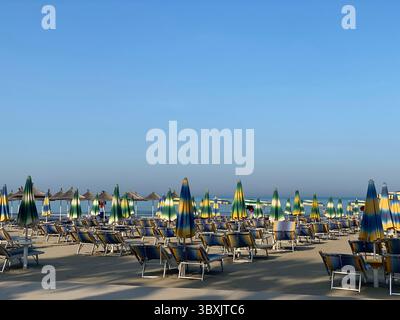 Ampia spiaggia sotto un cielo blu dominata da file su file di sedie a sdraio e ombrelloni con un motivo alternato di verde e giallo. Foto Stock