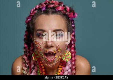 Close-up foto di una donna attraente con un multi-colore trecce acconciatura e luminoso per il make-up, guardando la telecamera dicendo qualcosa e in posa Foto Stock