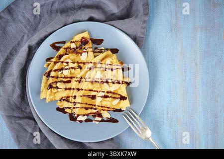 Due pancake con sciroppo di cioccolato, fiocchi di mandorle sul piatto, flussi di miele dal cucchiaio, vista dall'alto, spazio copia Foto Stock