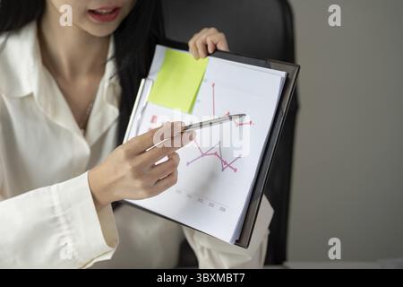 Una giovane donna impegnata presenta grafici fiscali, mostrando le sue capacità analitiche durante una discussione Foto Stock
