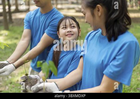 Un momento di gioia catturato come volontari di famiglia in camicie blu sorridono l'un l'altro tenendo in mano i giovani alberi, mostrando il loro impegno per l'ambiente Foto Stock