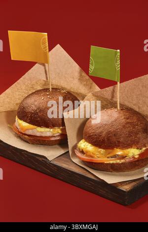 Due deliziosi hamburger con succose polpettine di pollo e manzo, pomodoro e formaggio in panini dorati decorati con bandiere colorate su stuzzicadenti, serviti in cr Foto Stock