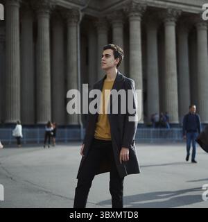 Bell'uomo elegante alla moda, bruna in un elegante cappotto grigio, sorge sulla strada nel centro storico di San Pietroburgo. Giovane con i capelli scuri Foto Stock