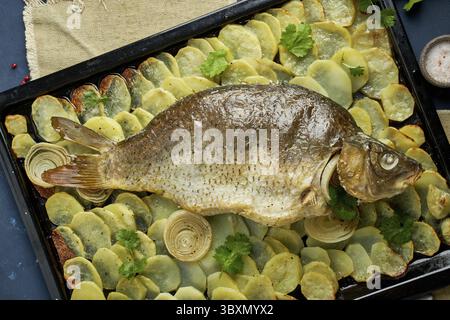 Carpa al forno, pesce intero dal forno con patate a fette su un vassoio grande Piatto tradizionale polacco europeo, adatto per un tavolo di Natale, vista dall'alto Foto Stock