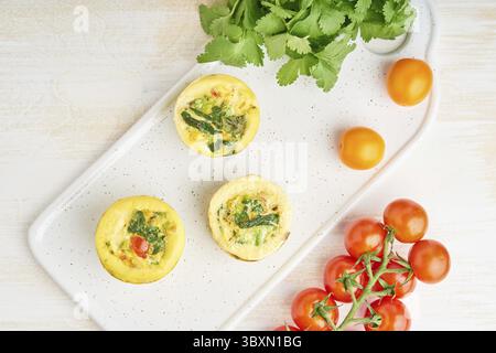 Muffin alle uova, paleo, dieta al cheto. Omelette con spinaci, verdure, pomodori cotti in piccoli stampi, vista dall'alto Foto Stock