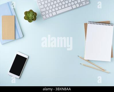 Vista dall'alto del moderno desktop blu per ufficio con blocco note vuoto, computer e smartphone. Mock up, spazio vuoto Foto Stock