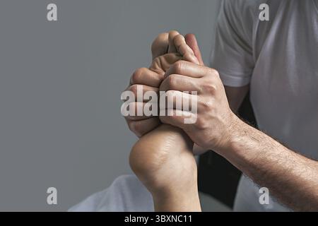 Mani massaggiatrici maschili che fanno un massaggio riflessologico sulle zone riflesse del piede femminile nel salone termale Foto Stock