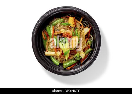 Appetitose tagliatelle di riso speziate con gamberi fritti, cozze, calamari e verdure servite in un recipiente nero, vista dall'alto isolata su sfondo bianco. T Foto Stock