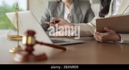 Avvocati che discutono questioni legali utilizzando un computer portatile e documenti in un ufficio moderno, concentrandosi sulla strategia e sulle soluzioni per i clienti Foto Stock