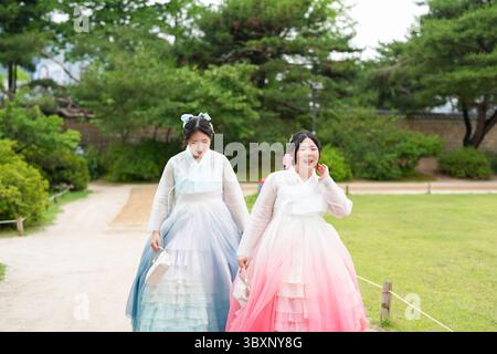 A giugno a Seul, due donne coreane sui vent'anni camminano tra piante lussureggianti e edifici tradizionali al Palazzo Gyeongbokgung, indossando l'affascinante a rosa Foto Stock