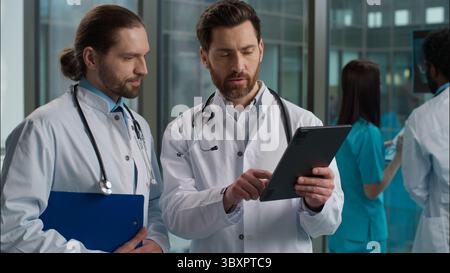 Esperto Caucasico due uomini medici medico chirurgo pediatra medico in grembiule stetoscopio che esamina il risultato del test di salute del paziente utilizzando Foto Stock